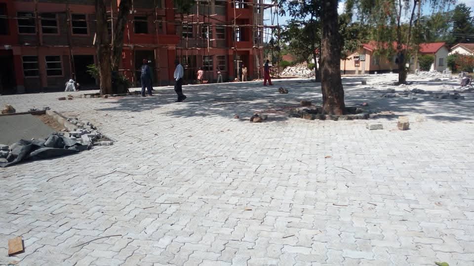 UCB Uni Pavers being installed at a large institutional compound in Kenya — workers paving a school or commercial facility with wavy interlocking concrete blocks