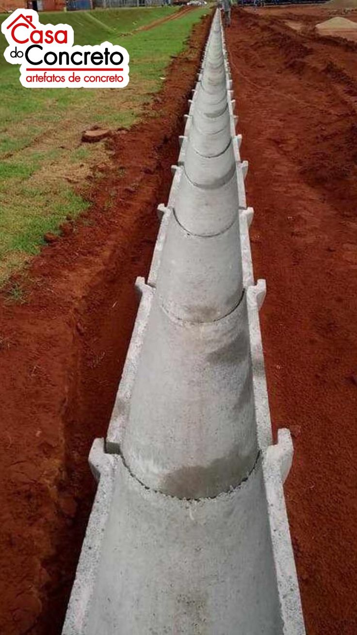 UCB Channels — long precast concrete half-pipe drainage channel being installed in a trench alongside red laterite soil by Unique Concrete Builders Kenya